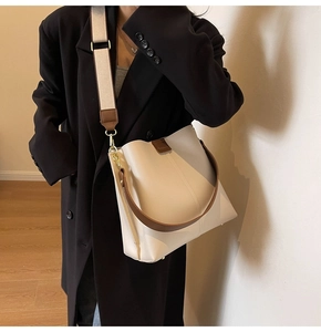 On-body view of cream bucket bag with wide strap and brown leather handle detail