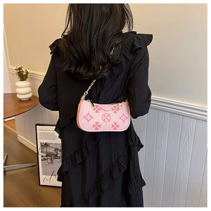 Pink shoulder bag with clover embossing and chain strap shown on model in cozy interior