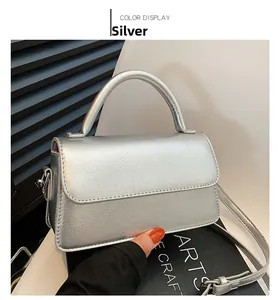 Detailed view of a silver metallic crossbody bag with top handle on a white chair