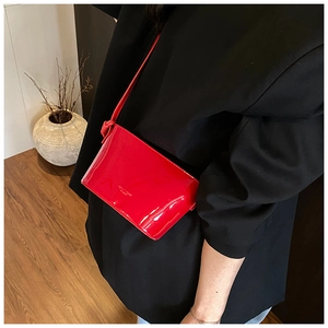 Détail d'un sac bandoulière rouge brillant porté avec une veste de blazer noire chic