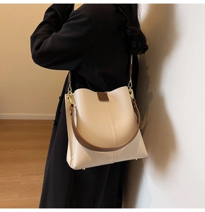 Detail of cream bucket bag with brown strap and gold metal feet on a wooden floor