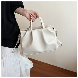 Detail der weichen cremefarbenen Ledertasche mit Plissee-Design und zylindrischen Griffen