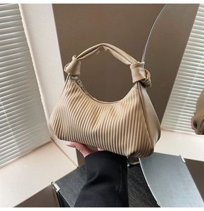 Detail of beige pleated pea bag featuring a stylish knotted handle and fine textures