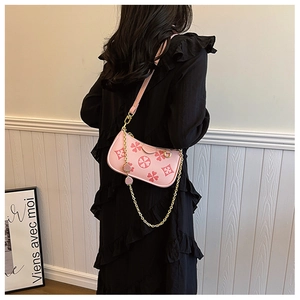 Pink shoulder bag with clover print and gold chain strap shown on a black dress