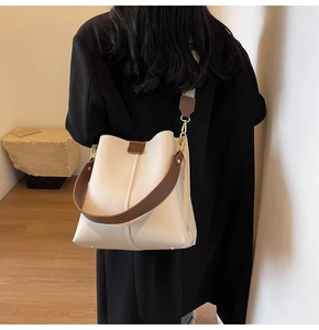 Detail of cream bucket bag showing wide brown strap and gold metal hardware hooks