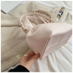 Detailed view of light pink pebbled leather bucket bag with gold hardware and cross stitching