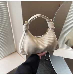 Detail of cream pleated leather handbag featuring vertical folds and a gold metal zipper