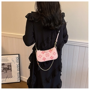 Pink embossed clover crossbody bag with gold chain strap worn over black dress
