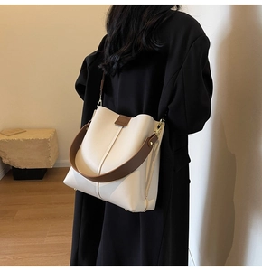 Detail of off-white bucket bag with brown wide strap and gold metal hardware accents