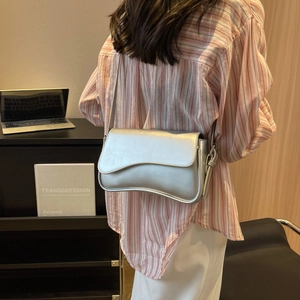 Silver metallic shoulder bag with wavy flap design shown on model in a modern office