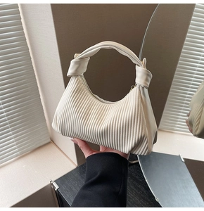 Detailed view of the cream-colored pleated handbag with a knotted handle detail