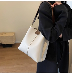 Detail showing white bucket bag with contrast brown wide strap and logo leather patch