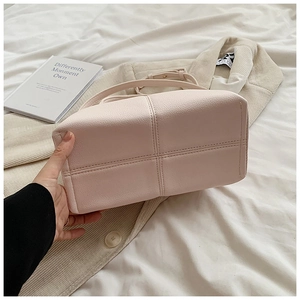 Detail of cross-stitched bottom design on light pink pebble leather handbag with strap