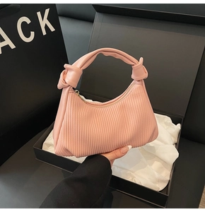 Detail of light pink pleated leather handbag with knot handle and golden zipper in gift box