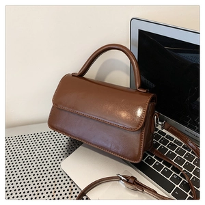 Detail of glossy brown square handbag with curved handle and adjustable strap on a laptop