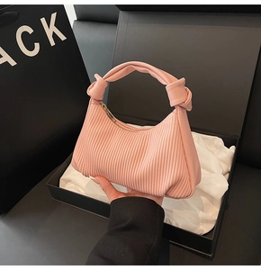 Detailed shot of pink ruched handbag with knotted handle and gold zipper in gift box