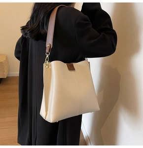 Close-up of beige leather bucket bag featuring wide brown strap and gold metal hardware