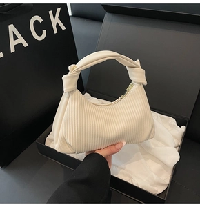 Detail of cream white pleated bag with a twisted knotted handle on black luxury packaging