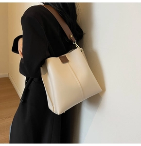 Detail of a large cream leather bucket bag with wide brown strap and gold hardware
