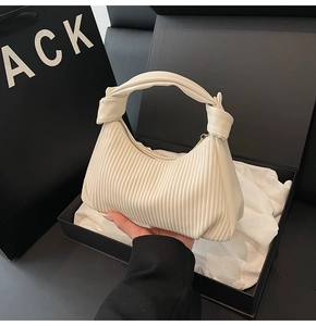 Detail of off-white pleated hobo bag with knotted handle and golden zipper on black background