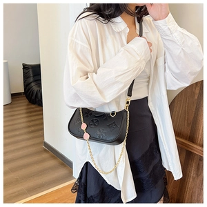 Detail of black crossbody bag with clover embossing and golden chain with heart charms