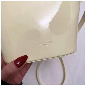 Gros plan du sac seau en cuir verni beige avec logo de la marque embossé sur la base