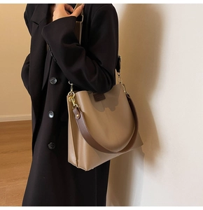 Detail view of large brown tote bag with wide strap and chain on fashion model