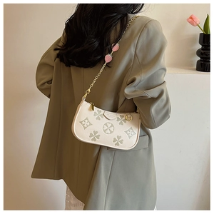 Detail of cream clover embossed baguette bag with strawberry charm on gold chain