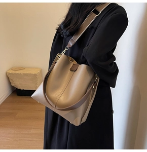 Detailed close-up of khaki leather bucket bag with wide shoulder strap on a model