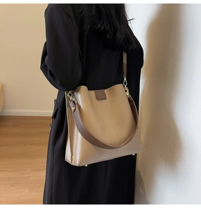 Side view of large khaki bucket bag with brown wide shoulder strap on a model
