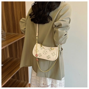 Detail of four-leaf clover print bag with gold chain strap on a green suit outfit