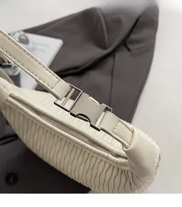 Close-up of white pleated shoulder bag featuring high-quality silver metal buckle hardware