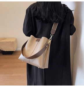 Detail of large beige bucket bag with dark brown straps and metallic bottom studs