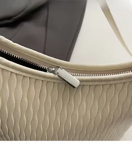 Close-up of beige shoulder bag featuring pleated ripple texture and smooth metal zipper