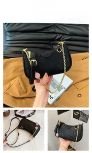 Detail view of black crescent bag with clover embossing and gold chain with strawberry charm
