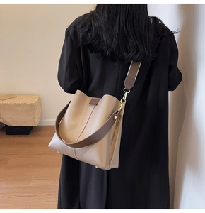 Detail of a large capacity beige bucket bag with a brown wide strap on a model's shoulder