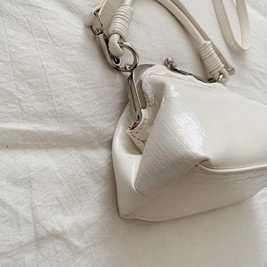 Detail view of a white vintage kiss-lock bag showing metallic clasp and woven strap accents