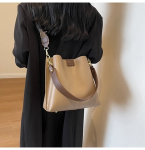 Detail showing khaki bucket bag with wide strap and gold hardware in home setting