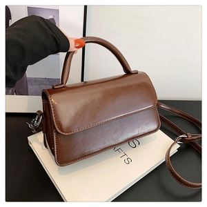 Detail view of glossy dark brown leather handbag with flap closure and firm top handle