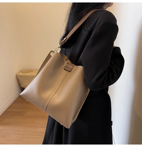 Close-up of the beige leather bucket bag showing wide strap and gold metal hardware