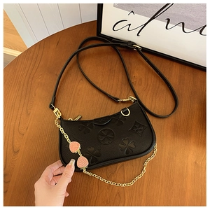 Close-up of black leather bag with embossed clover patterns and pink strawberry charms