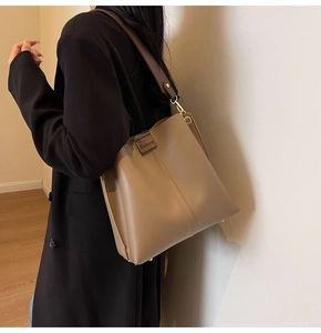 Detail of khaki bucket bag with wide brown strap and gold hardware on model