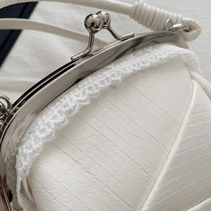 Detail of white kiss-lock handbag with crocodile texture and delicate lace trim