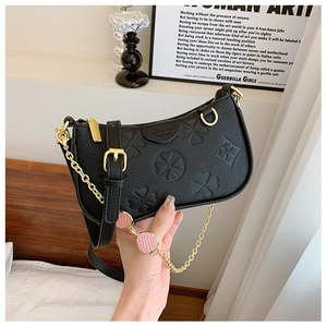 Detail of black embossed leather shoulder bag with strawberry charm chain and clover texture