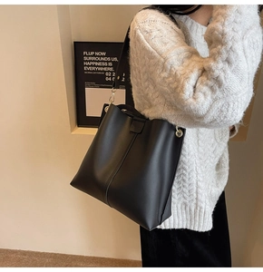 Detail of black matte leather tote bag featuring golden hardware and a wide shoulder strap