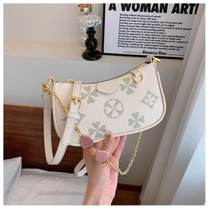 Detail of white crescent bag with strawberry charms and clover pattern chain