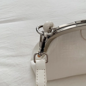 Detail of white crocodile embossed leather bag with silver metal frame and clasp closure