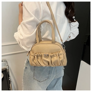 Detail of beige pleated handbag with metal clasp shown in a casual lifestyle setting