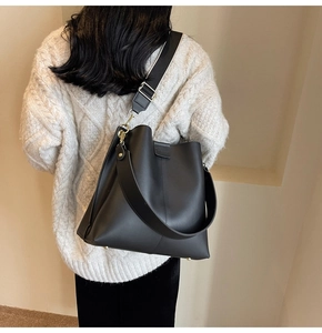 Close-up of black PU bucket bag featuring wide shoulder strap and metal feet detail