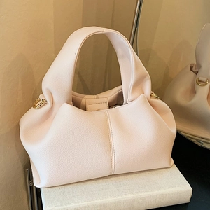 Sac nuage chic en cuir rose pâle avec ferrures dorées posé sur des livres blancs